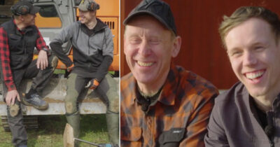 Gunde och Ferry Svan skrattar tillsammans, sittande på en grävmaskin och i närbild